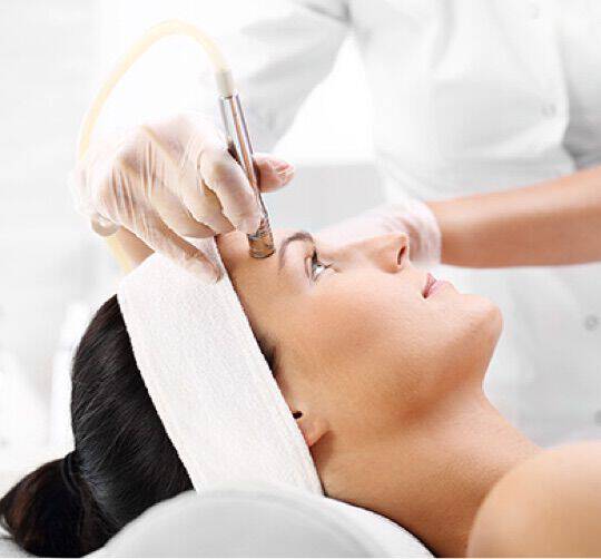 En kvinna ses från sidan medan en lakare utfor en ansiktsbehandling med en specialiserad apparat.